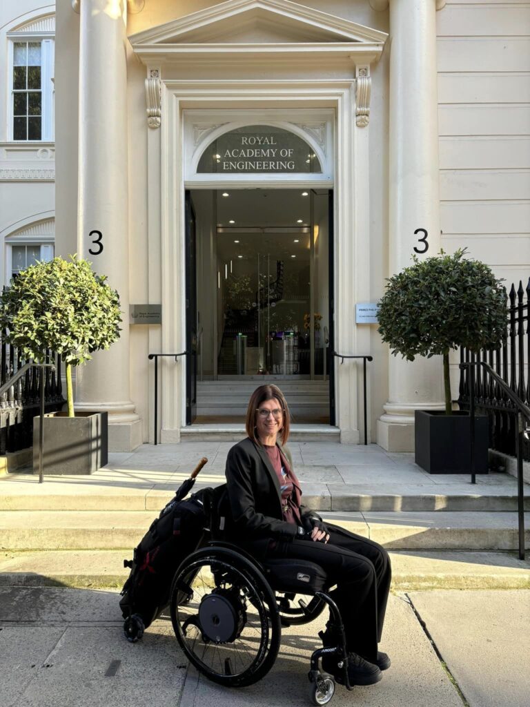 Katy Deacon sitting in a wheelchair outside the door to the Royal Academy of Engineering.